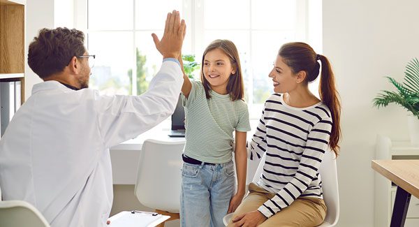 Physician giving high five to young girl while mom is smiling